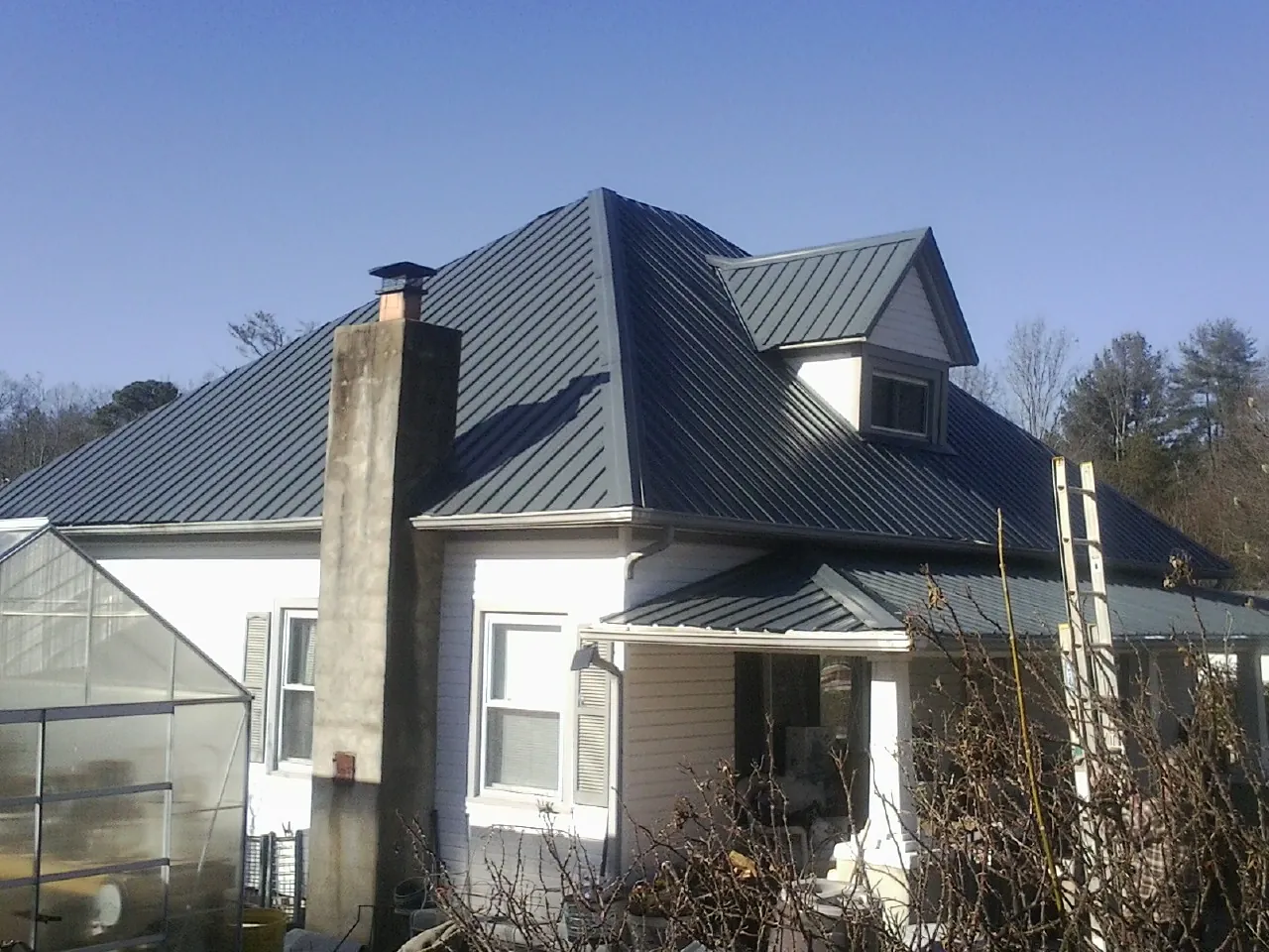 Dark blue standing seam metal roof on a white farmhouse with dormer — Slate & Tile Roof Repair by Roofing Brothers in Shambaugh