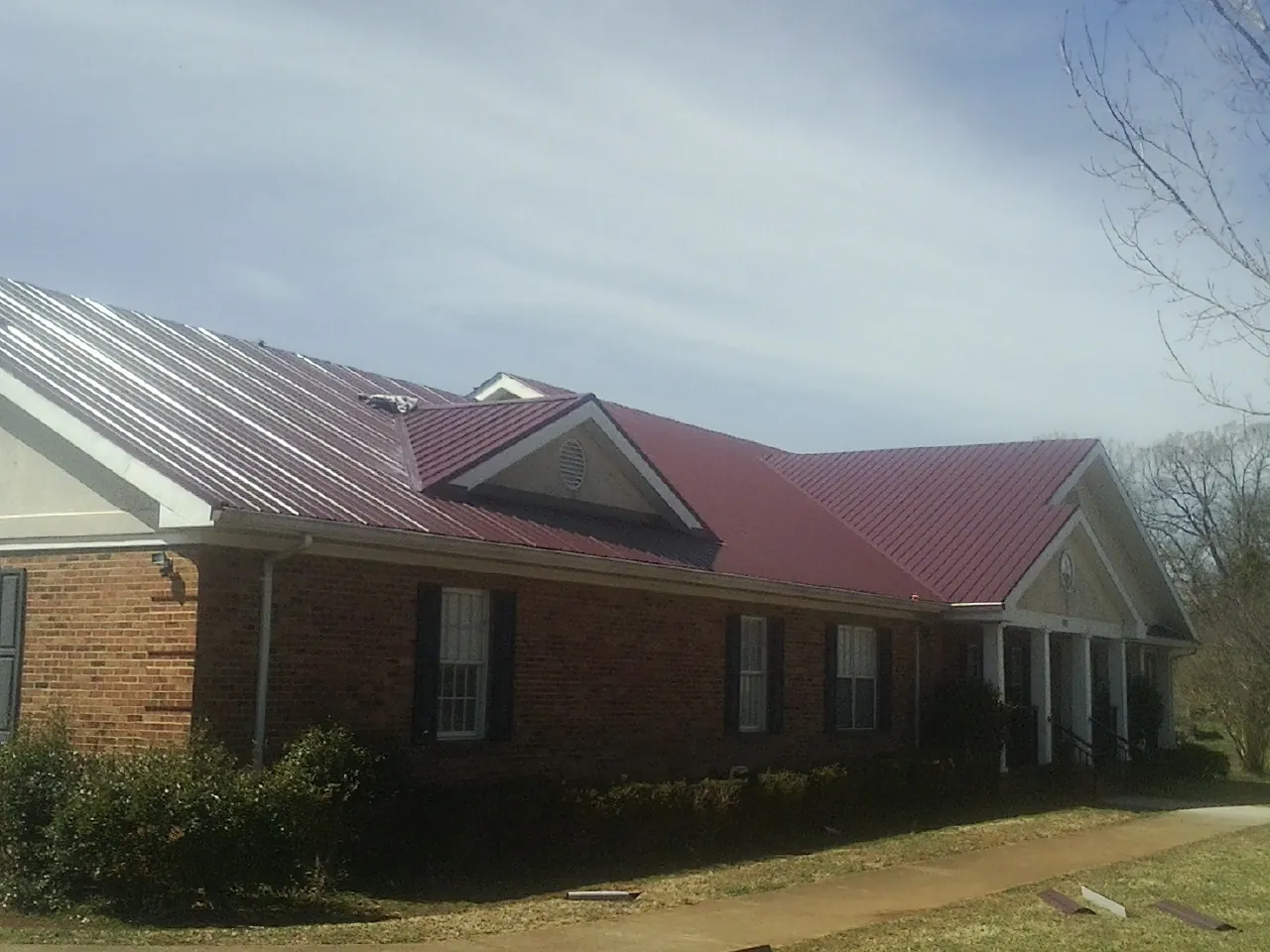 Red metal roof with gabled entries on a long brick building, from a Hail Damage Roof Repair job in Shambaugh