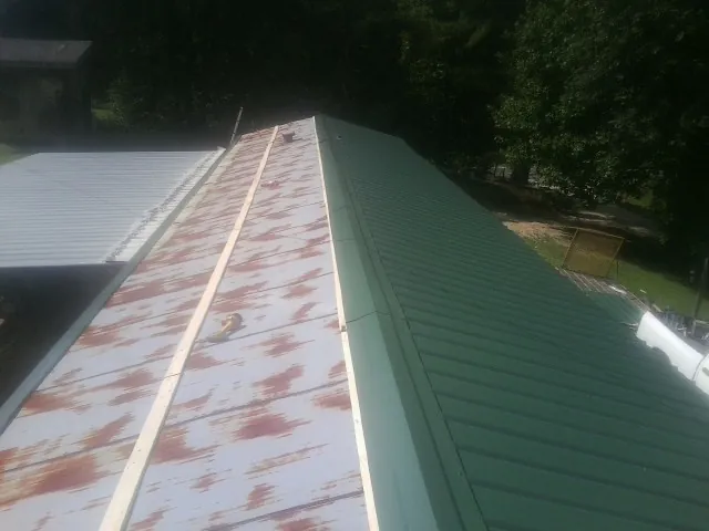 Old rusted panels beside newly installed green metal roofing — Wind Damage Roof Repair by Roofing Brothers in Shambaugh