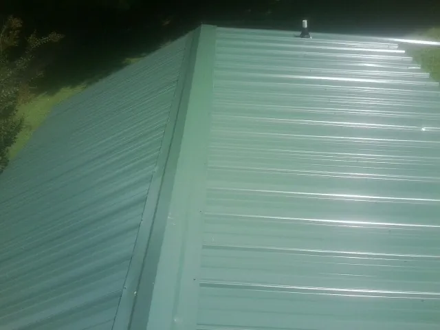 New green metal panels meeting at the ridge of a roof — Flat Roof Repair work by our crew in Shambaugh