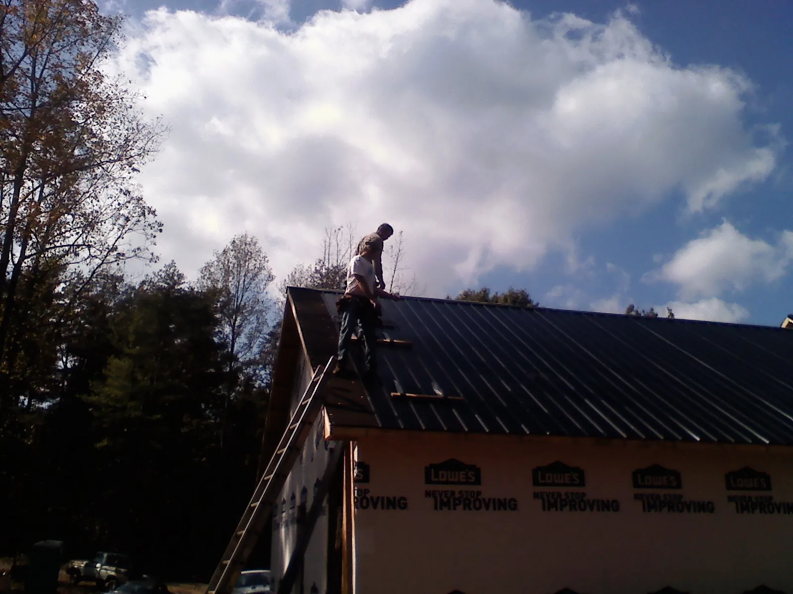 Roofer fastening dark metal panels high against a cloudy sky, from a Roof Inspection job in Shambaugh