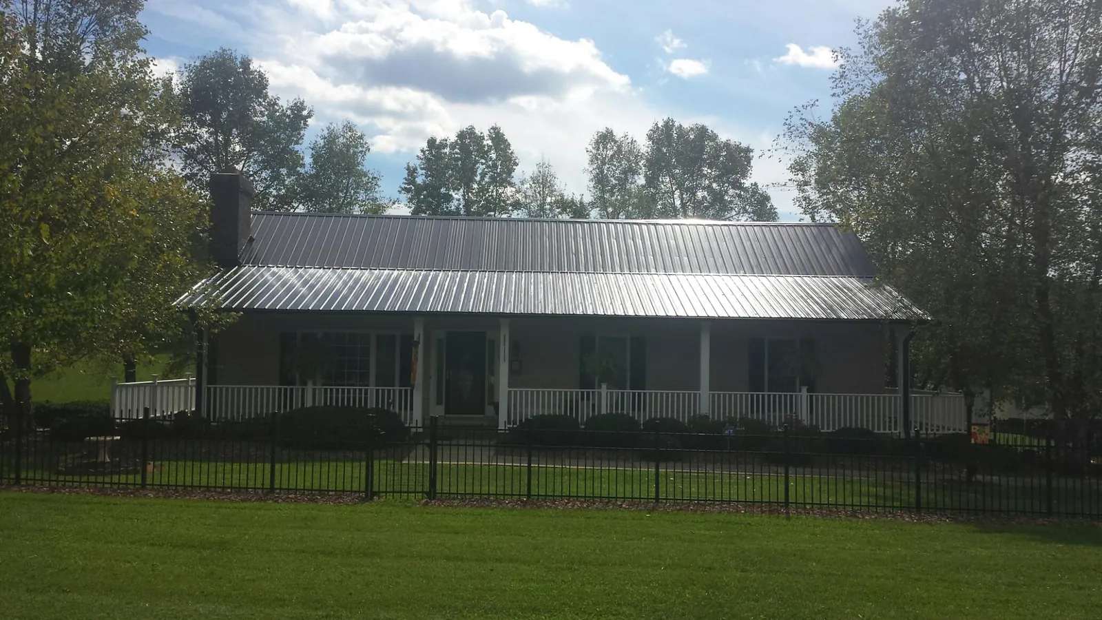 Gray metal roof on a brick ranch with a full width front porch — Gutter Guard Installation work by our crew in Shambaugh