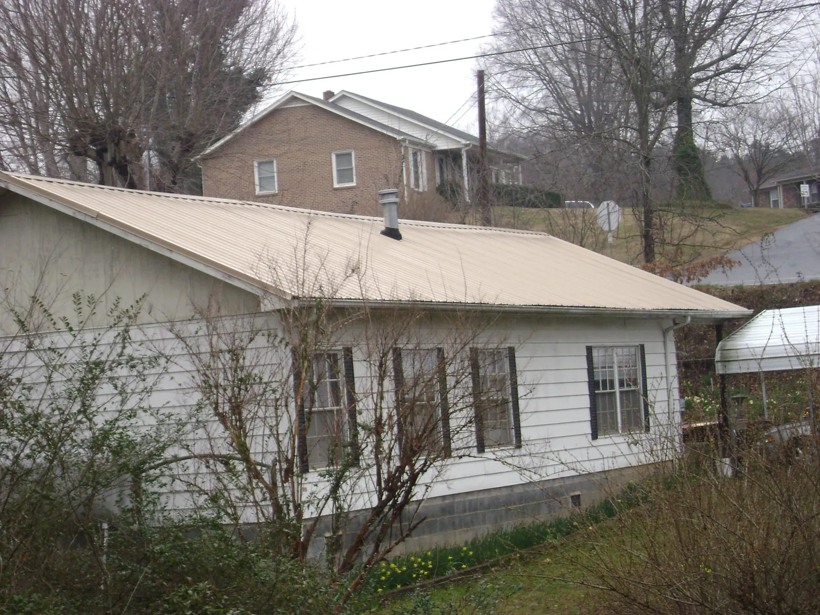 Tan metal roof on a white sided house set into a hillside — Commercial Roofing by Roofing Brothers in Shambaugh