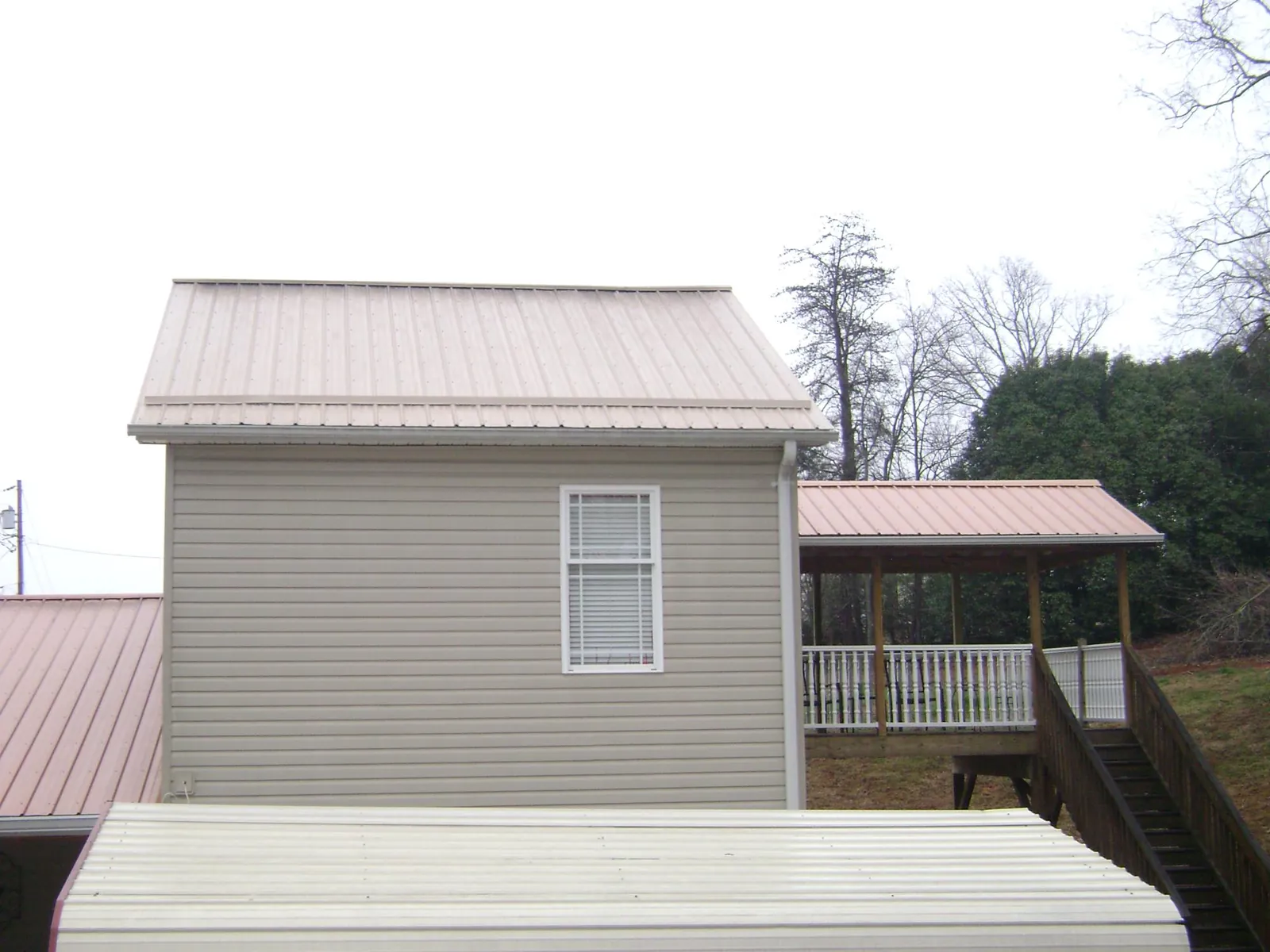 Tan metal roofs on a two story addition and attached porch, from a Roof Replacement job in Shambaugh